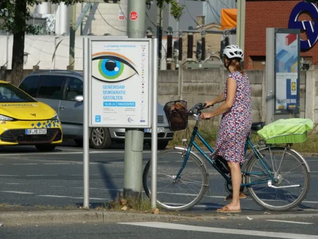 veranstaltungsplakat für städtisches präventionsprojekt an straße mit autos und radfahrer